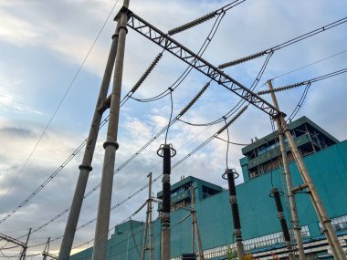 Yüksek voltajlı elektrik hatları, bulutlu gökyüzünün altında sanayi bölgesi boyunca uzanıyor.