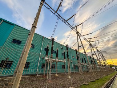 Yüksek voltaj hatları, çitleri ve renkli günbatımı gökyüzü boyunca inşa edilen bir elektrik santrali..