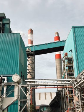 Endüstriyel fabrika manzarası sergilenen soğutma kuleleri, turkuaz binalar ve metal borular