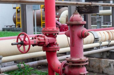 Detaylı bir yakın plan çekimde, bir dizi canlı kırmızı endüstriyel boru ve temel altyapı ve güvenlik önlemlerini temsil eden bir yangın musluğu sergileniyor. Bu resim karmaşık ağ görüntülerini yakalar