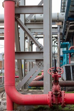 Bu resim, kırmızı borular ve metal yapılardan oluşan karmaşık ağın vurgulandığı endüstriyel bir boru hattı sisteminin yakın çekimini gösteriyor. Odak noktası mimari tasarım ve mühendislik.,