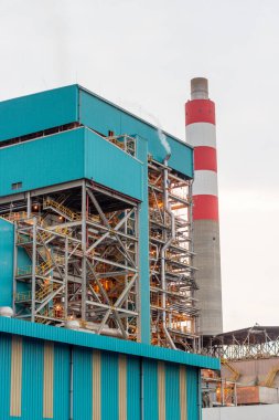 Bu görüntü, enerji üretimini ve teknolojik altyapıyı sembolize eden önemli bir bacaya sahip bir endüstriyel kompleksi yakalıyor. Karmaşık yapılar ve yüksek yapılar,