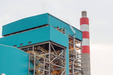 Yüksek kırmızı ve beyaz çizgili baca yapısına sahip endüstriyel elektrik santrali manzarası, ilgili mavi binalar ve elektrik santralini çevreleyen altyapı...