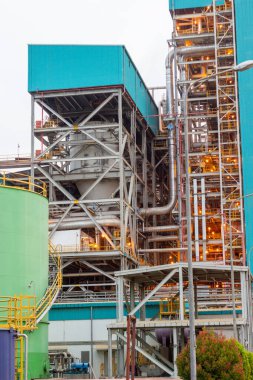 Bir elektrik santralinin karmaşık altyapısını gösteren detaylı bir çekim. Borular, çelik yapılar ve mimari elementler modern enerji üretiminin karmaşıklığını ve ölçeğini gösteriyor.