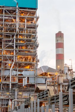 Bu resim, metal yapılar, borular ve makinelerden oluşan bir ağ ile genişleyen bir endüstriyel kompleksi içerir. Sahne, rafineri setiyle modern imalatın boyutunu ve karmaşıklığını yakalıyor.