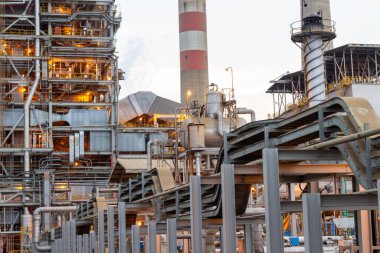 Bu fotoğraf, metal yapılar, borular ve parlak bir gökyüzü altında yükselen bacalardan oluşan bir ağı gösteren genişleyen bir endüstriyel kompleksi yakalıyor. Görüntü karmaşık mimariyi vurguluyor.