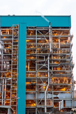 Bu görüntü engin bir endüstriyel rafineri kompleksini yakalıyor, gökyüzüne karşı onun karmaşık borular ağını ve yapısal iskeletini vurguluyor. Rafineride karmaşık makineler ve