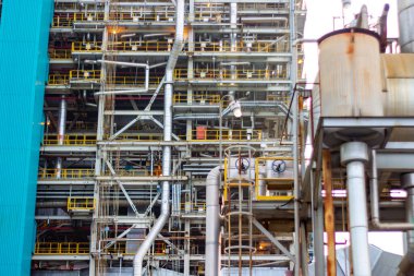 Detaylı bir çekim, büyük bir sanayi kompleksi içindeki karmaşık boru hatları ve metalik yapıları yakalıyor. Görüntü modern sanayinin karmaşıklığını ve ölçeğini gözler önüne seriyor.