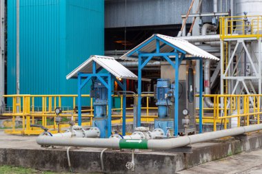 Bu görüntüde mavi motor kapakları ve geniş bir boru ve vana ağına sahip bir pompalama sisteminin yer aldığı bir sanayi sitesi görülüyor. Sahne karmaşık mekanik ve mühendisliği vurguluyor.