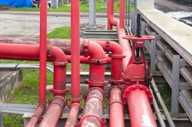 Kırmızı borular, vanalar ve metal bağlantılardan oluşan karmaşık bir endüstriyel boru sisteminin ayrıntılı bir görüntüsü. Resim, çeşitli alanlarda kullanılan karmaşık altyapı ve ekipmanları sergiliyor