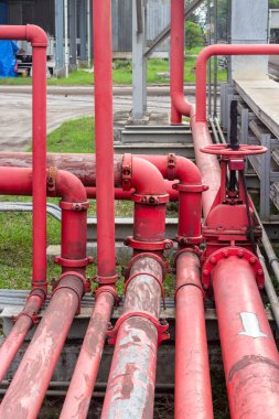 Endüstriyel ayar sistemindeki karmaşık kırmızı boruların ayrıntılı bir çekimi birbirine bağlı borular, vanalar ve metal yapılar sergiliyor. Görüntü, sağlam mimariyi ve temel rolü vurgular.