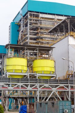 Bu görüntü, büyük sarı depolama tankları, büyük mavi bir bina ve karmaşık metal yapılardan oluşan bir endüstriyel kompleks yakalar. Sahne, modern dünyanın boyutunu ve karmaşıklığını gözler önüne seriyor.