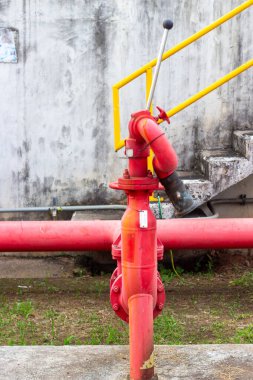 Ön planda belirgin kırmızı bir yangın musluğu duruyor, dokulu bir duvara ve parlak sarı korkuluklara karşı. Bu sahne kentsel altyapının önemli bir bileşenini vurguluyor,