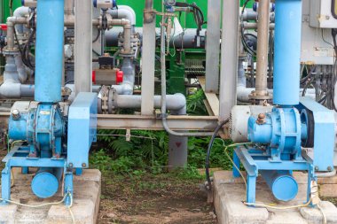 Görüntü, çeşitli sanayi süreçleri için gerekli karmaşık altyapı ve mekanik bileşenleri vurgulayan endüstriyel üfleyiciler ve karmaşık bir boru sistemi sergiliyor. Mavi boyalı olan