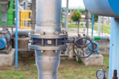 Sürgülü eklemler ve basınç göstergesiyle tamamlanmış kapakçık ve kanatlı bağlantıların yer aldığı endüstriyel bir boru hattının yakın çekimi. Dekor, açık hava endüstriyel bir ortam.