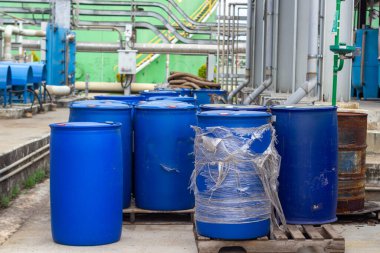 Kimyasal madde depolamak için kullanılan endüstriyel bir tesiste mavi plastik varillerin bulunduğu bir manzara. Fıçılar ahşap paletlere yerleştirilmiş, atık yönetimi ve çevre düzenlemeleri sergileniyor.