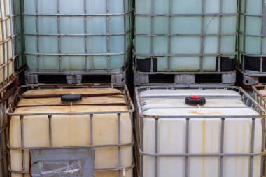 Bu resim, ahşap paletler üzerinde orta büyüklükteki konteynırların (IBC 'lerin) istiflenmiş düzenlenmesini içerir. IBC 'ler genellikle endüstriyel kimyasalları ve sıvıları depolamak ve taşımak için kullanılır. Şey...