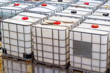 Paletlerin üzerine yığılmış çok sayıda orta büyüklükteki konteynırı (IBC 'leri) gösteren yakın plan bir fotoğraf, sıvı depolama ve ulaşım sistemini gösteriyor. Görüntü endüstriyel uygulamayı vurguluyor