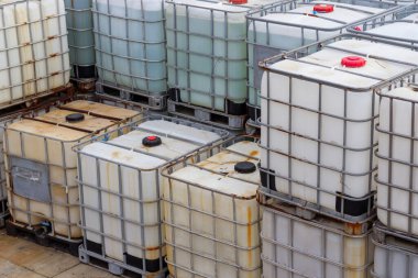 Metal kafesler ve sıvı veya malzeme taşımacılığı için kullanılan plastik tanklar ile bir depo alanında düzenlenmiş sıkıca paketlenmiş bir endüstriyel kap grubu. Bu ara konteynırlar...