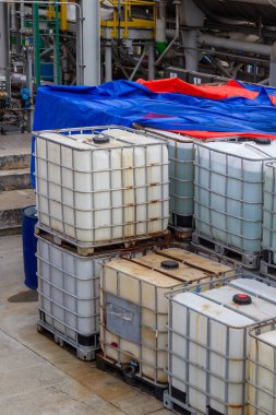 Görüntü endüstriyel konteynırların düzgün bir şekilde istiflenip depolandığını, kimyasal bir tesiste dağıtılmaya hazır olduğunu gösteriyor. Toptan malzemelerin taşınması ve depolanmasında güvenlik ve verimliliği vurguluyor..