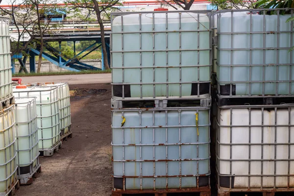 Görüntü, açık hava endüstriyel depolama sahasında birçok üst üste konteynır (IBC) gösteriyor. Bu büyük kaplar, genellikle toplu sıvıları taşımak ve depolamak için kullanılır.