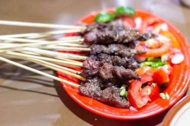 Bu görüntü, mükemmel ızgara sığır eti şişleri ile lezzetli bir yemeğin özünü yakalıyor. Canlı kırmızı tabak sulu domateslerle güzel bir tezat oluşturuyor. Bu aşçılık zevki...