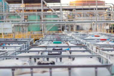 Görüntü, bir imalat tesisinde sıvı depolamak için sıra sıra beyaz endüstriyel konteynırlar içeriyor. Konteynırlar arka planda karmaşık bir boru ve tank ağı ile sıralanmış.