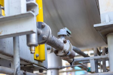 Endüstriyel bir boru hattı ağının yakın görüntüsünde, endüstriyel üretim tesisi bünyesinde gerekli sıvı veya gazları taşıyan metalik boru valflerinin ve kanatların karmaşık bir konfigürasyonu sergileniyor..