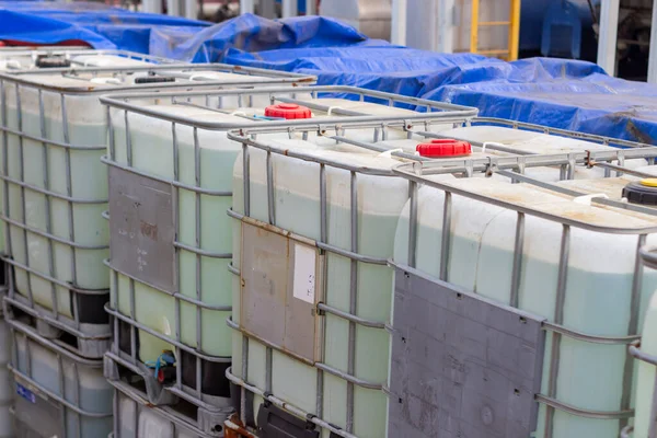 Endüstriyel bir alanda büyük sıvı konteynırların depolanması. Mavileştirilmiş konteynırlar şeffaf ortamla doldurulur ve taşınmaya ve depolanmaya hazır metal kafeslerle güvenceye alınır.