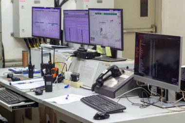 Bir kontrol merkezinde birden fazla monitör, çeşitli telsiz ve sabit telefon bulunur. Teknik gözetim ve gerçek zamanlı izleme operasyonları için odaklanmış bir çalışma alanı oluşturulur.