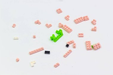 Temiz beyaz bir yüzeye karşı pembe, yeşil, siyah ve beyaz tonlarında çeşitli boyut ve şekillerde dağılmış yapı taşları, oyuncu düzenleme ve renk göstermektedir.