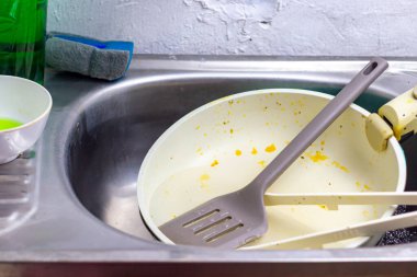 Kirli bulaşık ve yemek pişirme aletleriyle dolu bir mutfak lavabosu, telaşlı bir yemek oturumu ve sonrasında ev ortamında temizlik ve temizlik ihtiyacını akla getiriyor..