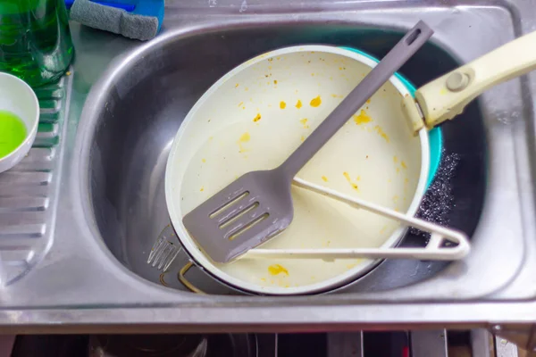 Kirli yemek takımları ve çatal bıçaklarla dolu dağınık paslanmaz çelik bir lavabo yemek ve yemek hazırlığından sonra günlük bulaşık yıkama angaryasını sergilemeyi bekliyor..