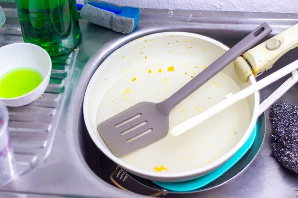 Kirli bir tava, spatula ve diğer mutfak gereçleri ile dolu paslanmaz çelik bir lavabo ev işlerinin ve günlük ev idaresinin yükünü gösteriyor..