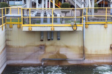 Boruları ve sarı korkulukları olan sanayi yerleşim tankı su arıtma sürecini gösteriyor..
