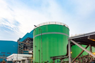 Bulutlu bir gökyüzünün altında canlı yeşil depolama tankı barındıran sanayi manzarası