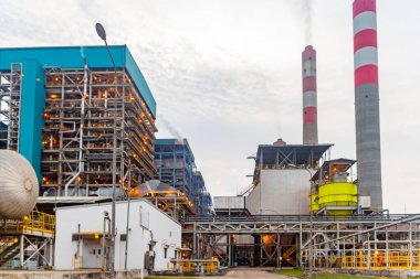 Hava kararınca bulutlu gökyüzüne duman yayan yüksek bacalı sanayi enerji santrali..