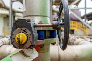 Endüstriyel boru hattı sisteminde yıpranmış bir ayarda kapakçık mekanizması, tekerlek ve borular gösteriliyor