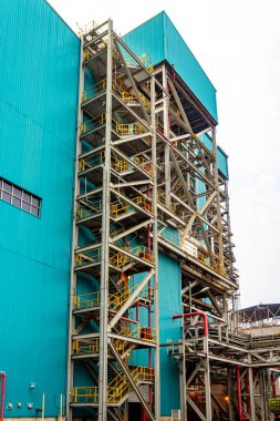 Dış mimari, canlı mavi sanayi binasına karşı çelik yapılar sergiliyor.