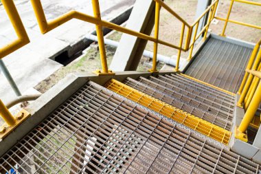 Metal parmaklıklı merdivenler ve sarı korkuluklar güvenliği temsil ediyor..