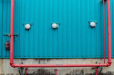 Turkuaz duvar üç alarm ve kırmızı borular gösteriyor. Kontrast ve görsel ilgi yaratıyor..