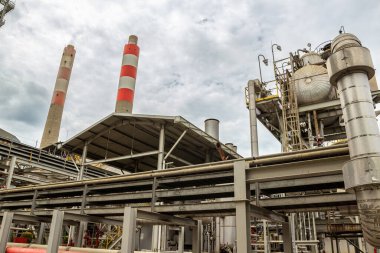 Karmaşık boru sistemleri, çelik yapıları ve yüksek çizgili bacası olan endüstriyel tesis.