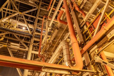 Fabrikada sıcak ışıkta aydınlanan karmaşık endüstriyel boru hatları ve metal yapı
