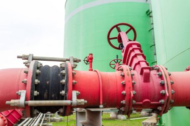Dışarıda vanaları, eklemleri ve yeşil depolama tankları olan büyük kırmızı endüstriyel boru hattı sistemi..