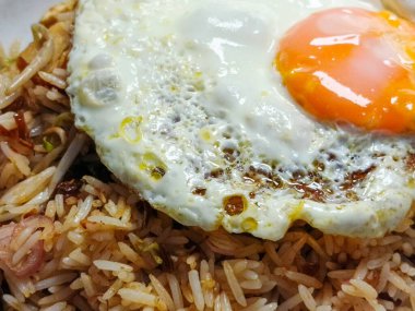 Yakından bakınca, üzerinde kusursuz pişmiş güneşli bir yumurta bulunan lezzetli bir tabak pilav görünüyor. Yemek davetkar ve lezzetli bir aşçılık ürünü. Parlak renkler.