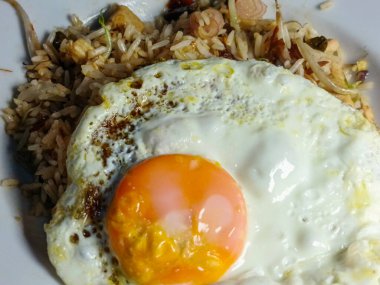 Bu resimde nefis bir tabak kızarmış pilav var, mükemmel bir şekilde pişmiş yumurta ile tamamlanmış. Yemek, bir karışımın basitliğini ve memnuniyetini gösteren dokular ve tatlar sunuyor.