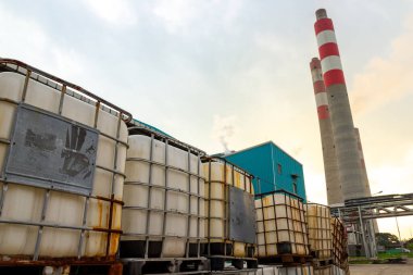 Dışarıda günbatımına karşı yükselen uzun bacalı sanayi konteynırları var..