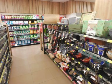 İyi stoklanmış bir süpermarkette yakalanan resim, mutfak eşyaları ve mutfak eşyalarıyla dolu bir koridorda bir görüntü sunuyor. Her iki taraftaki raflarda çeşitli ürünler sergileniyor.