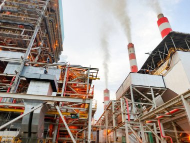 Bu görüntü, borular, yapılar ve bacalardan oluşan ağıyla bir enerji santrali yakalıyor duman salıyor, endüstriyi ve enerji üretimini sembolize ediyor, çevresel kaygıları vurguluyor ve