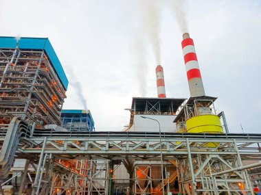 Bu fotoğraf, gökyüzüne buhar yayan dumanlı büyük bir endüstriyel kompleksi gösteriyor. Görüntü, modern sanayi tesislerinin ölçeklerini ve karmaşıklığını vurguluyor,